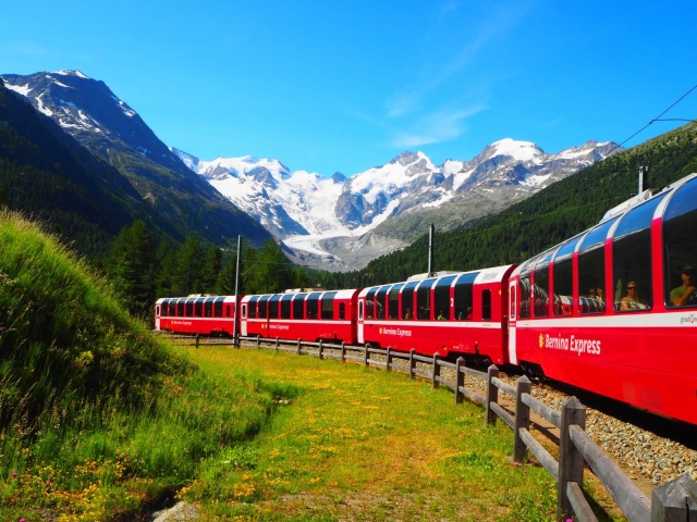 雪をかぶったアルプスの山々を背に、草原の中を走る赤い登山列車